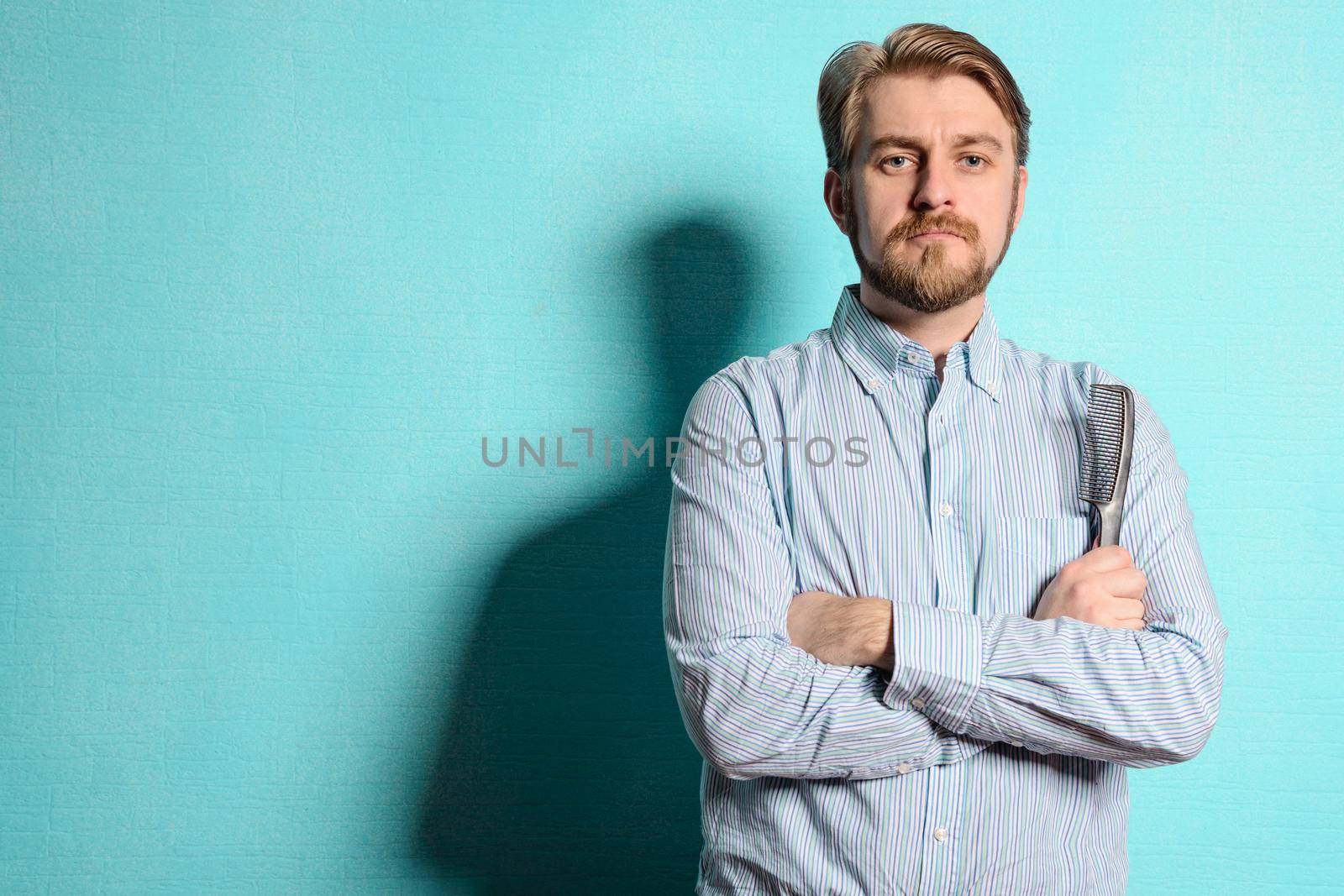 Portrait of young hairstylist standing against blue background.