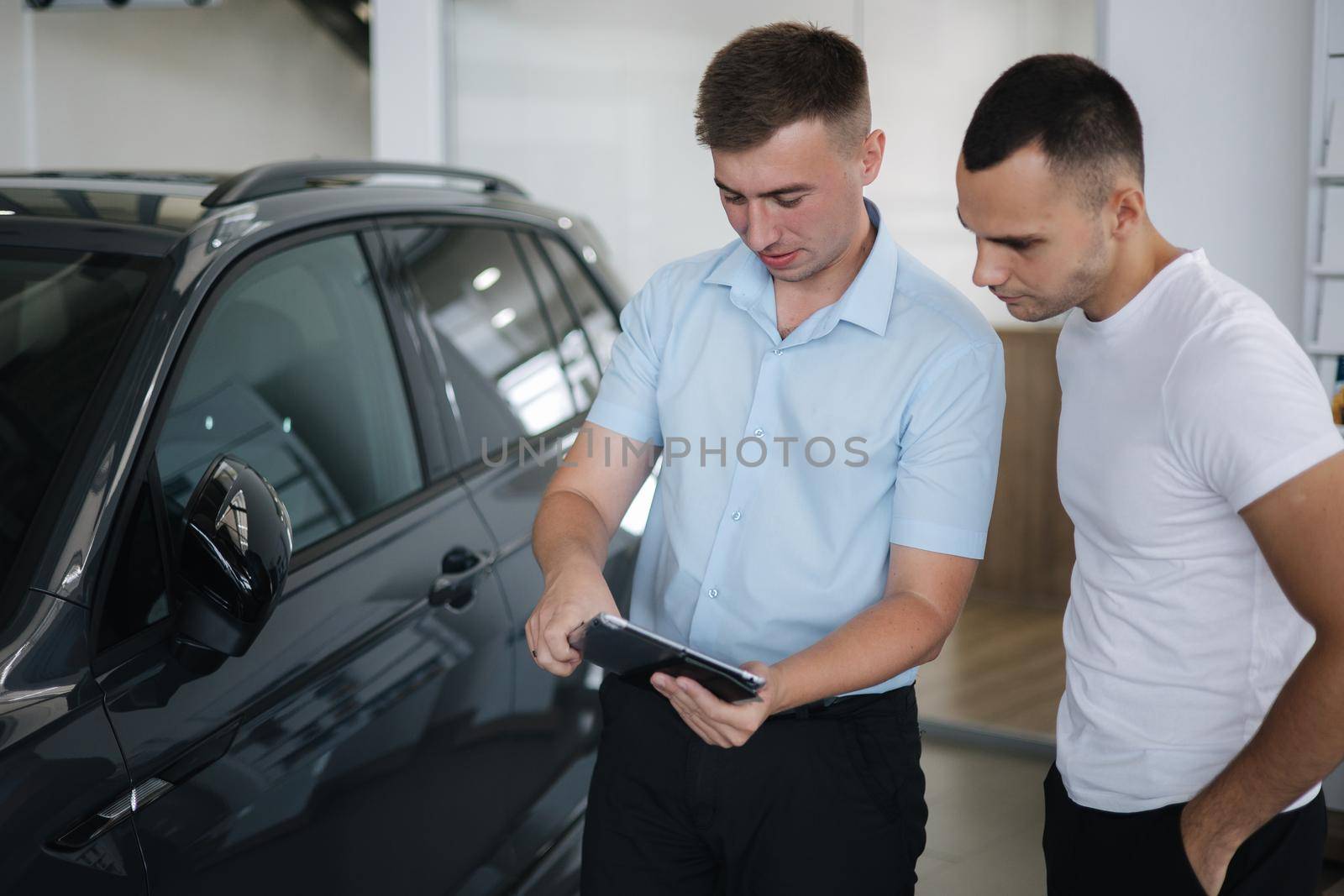 Salesperson selling cars at car dealership. Man choosing car in car showroom,