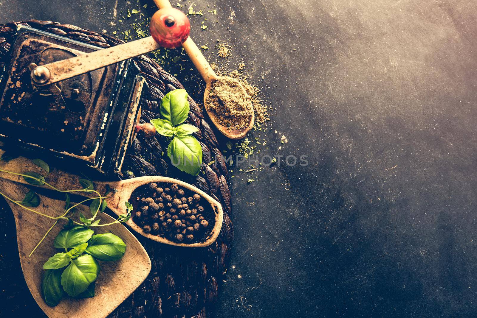 old mill and wooden spoons with spices on a black table