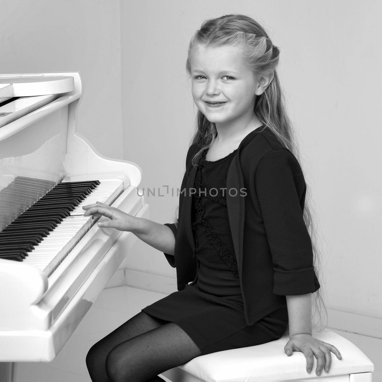 Beautiful little girl playing on white grand piano. Black and white shot of pretty long haired girl sitting at piano in living room. Cute child learning to play music instrument