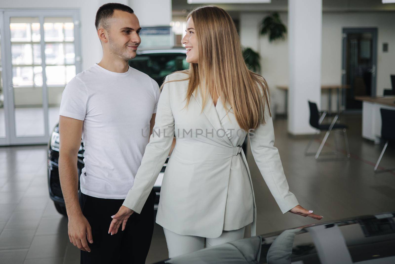 Happy woman hug his husband afrer buying car in car showroom. Man and woman buy new car by Gritsiv