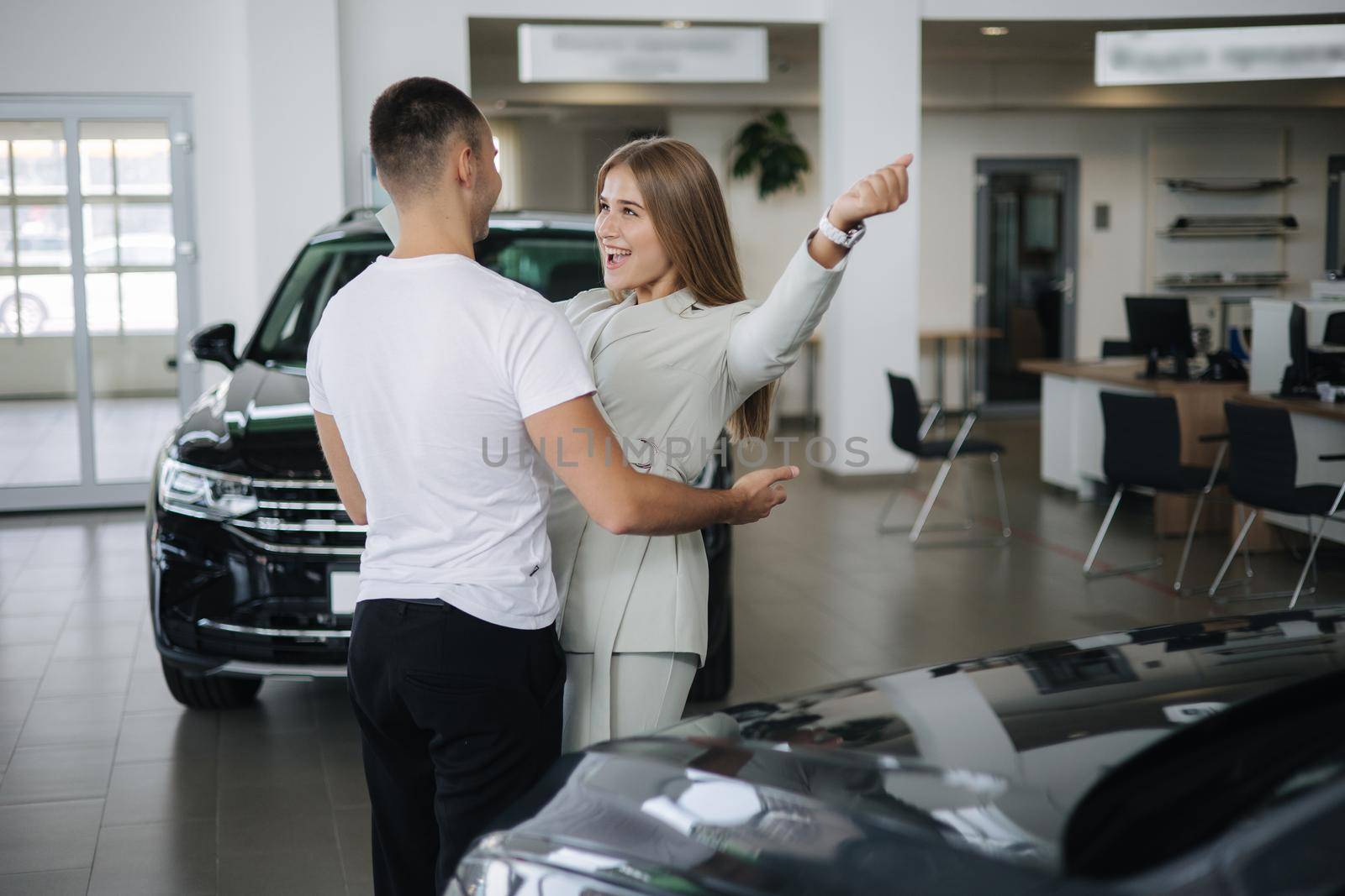 Happy woman hug his husband afrer buying car in car showroom. Man and woman buy new car.