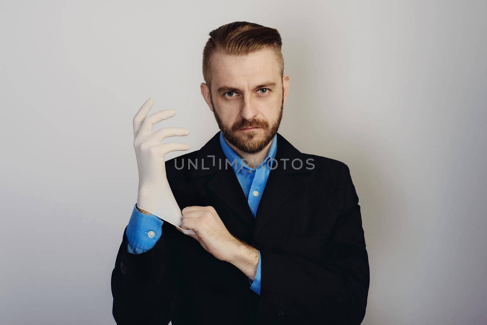 stylish bearded businessman in suit and blue shirt puts on medical glove on gray background