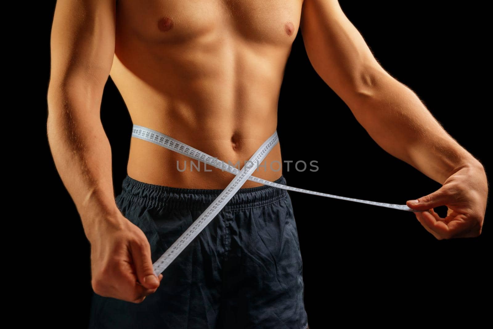 Unrecognizable muscular man is measuring waist with tape