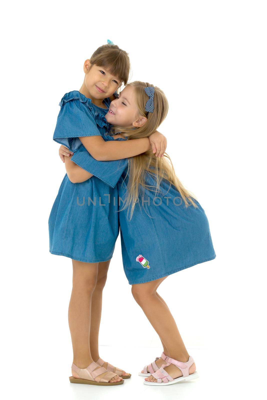 Two happy girls hugging each other. Adorable girls dressed in the same dresses having fun together on isolated white background.