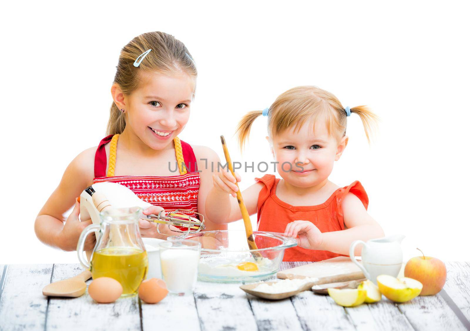 two smiling little sisters cooking isolated on a white background