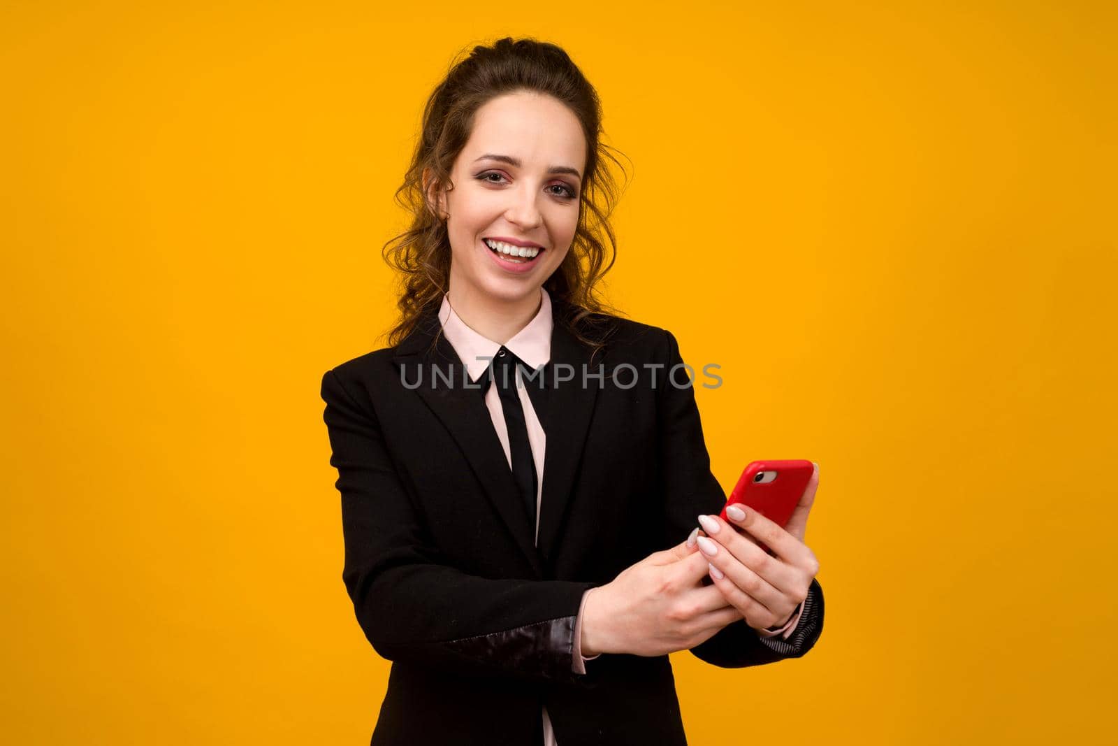 Photo of pleased young woman posing isolated over yellow wall background using mobile phone. - image