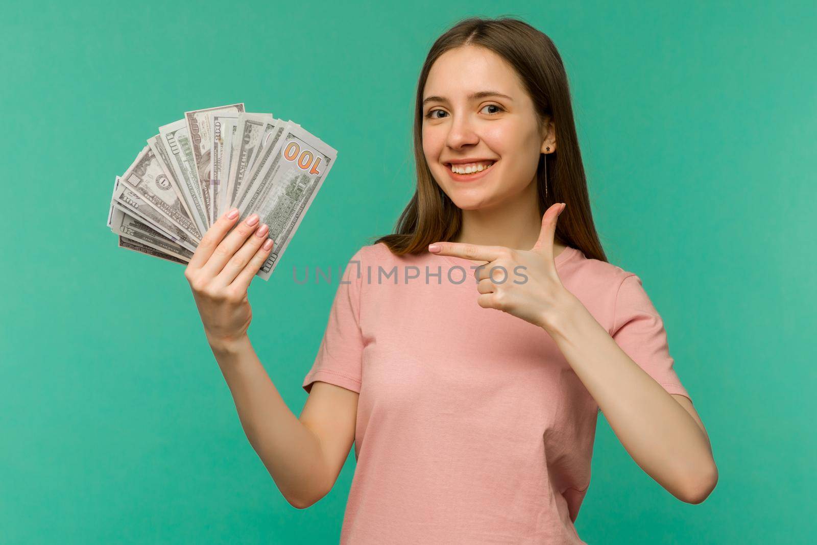 Portrait of a cheerful young woman holding money banknotes and celebrating isolated on blue background