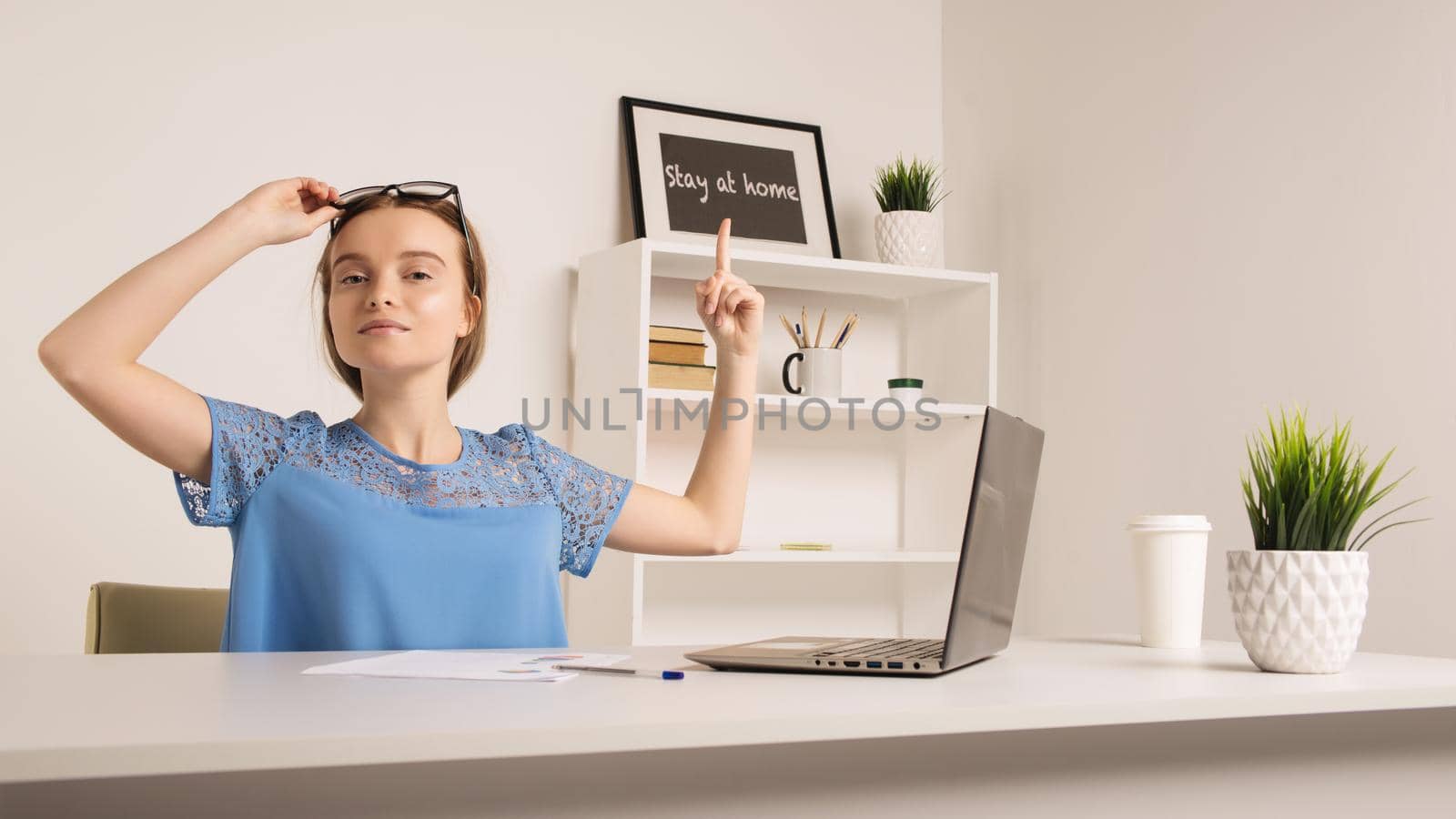 Cute girl in the office shows a finger to the inscription stay at home. by zartarn