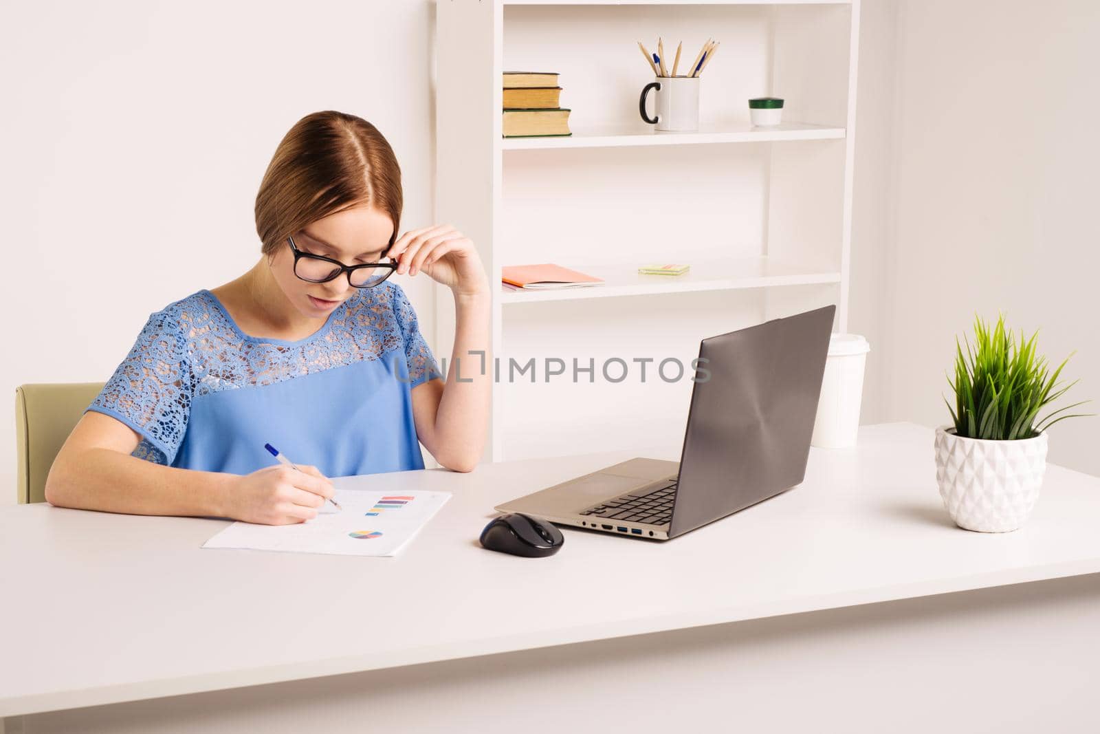 happy american young woman sitting at table with laptop computer and books at home by zartarn