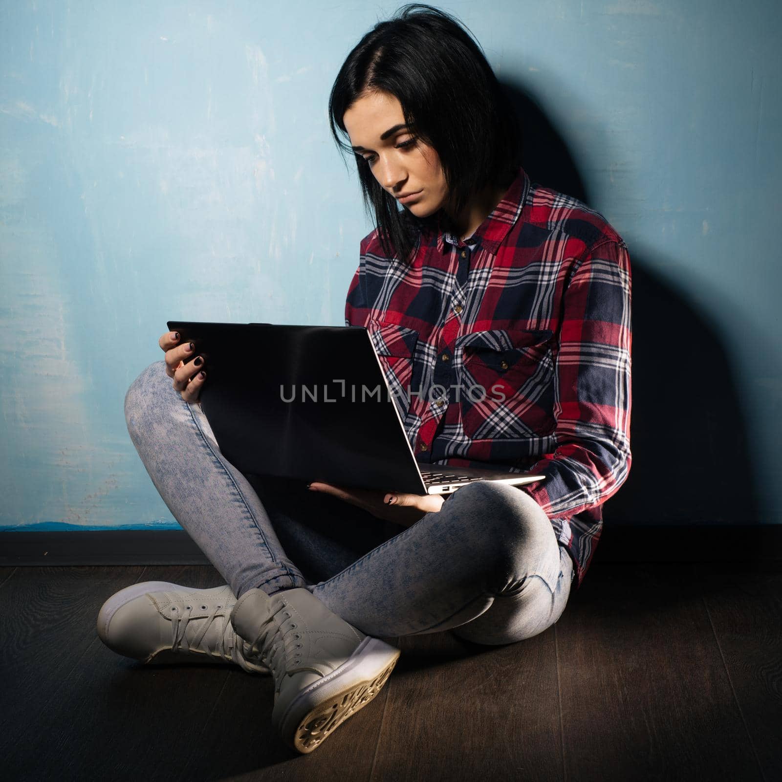 Young sad girl suffering from dependence on social networks sitting on the floor with a notebook