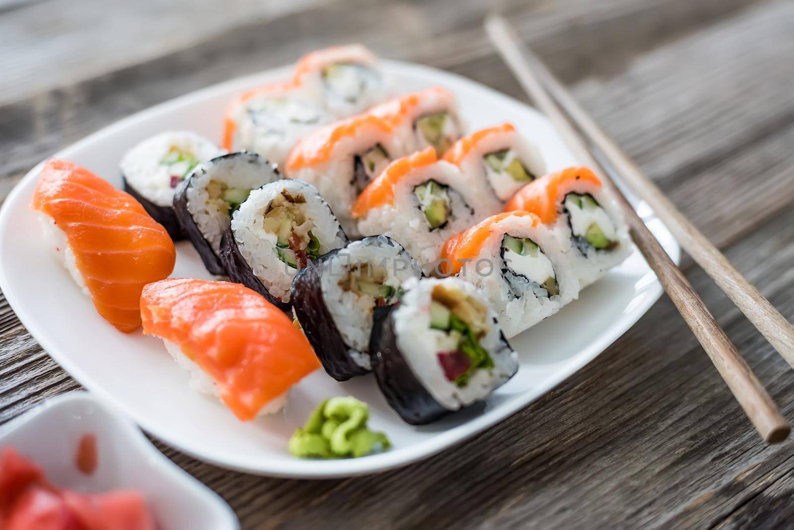 various Japanese sushi on white plate with chopsticks on wooden background