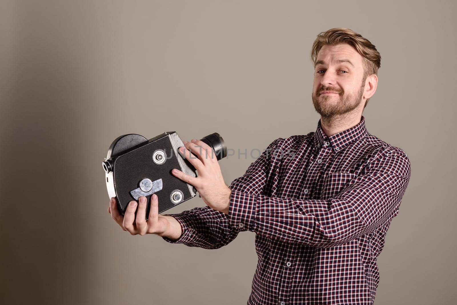 Young attractive cameraman in a plaid shirt takes himself off to an old movie camera.