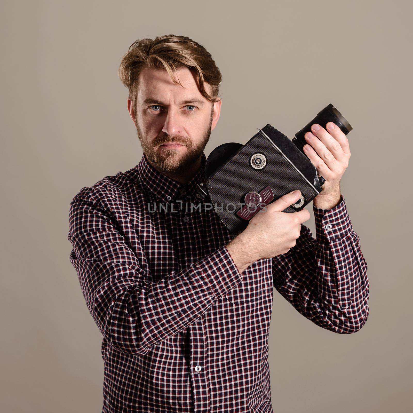 Stylish attractive cameraman in a checkered shirt holds in the hands of an old movie camera.