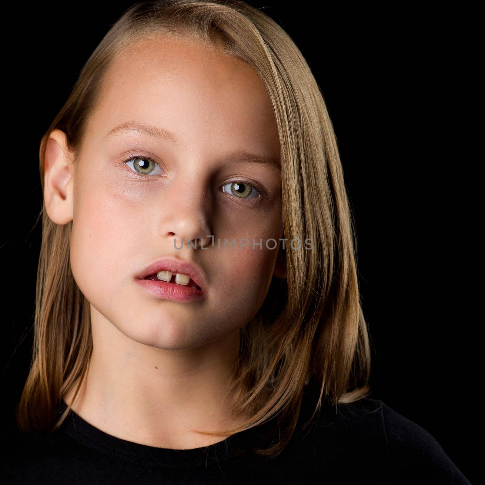Close-up portrait of a beautiful blonde teenage girl in a black t-shirt on a black background. by kolesnikov_studio