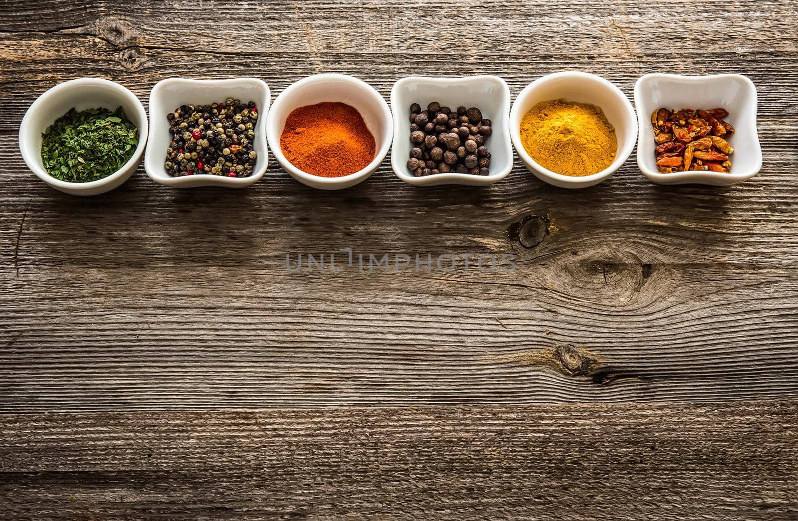 aromatic spices in bowls in horizontal row on wooden background