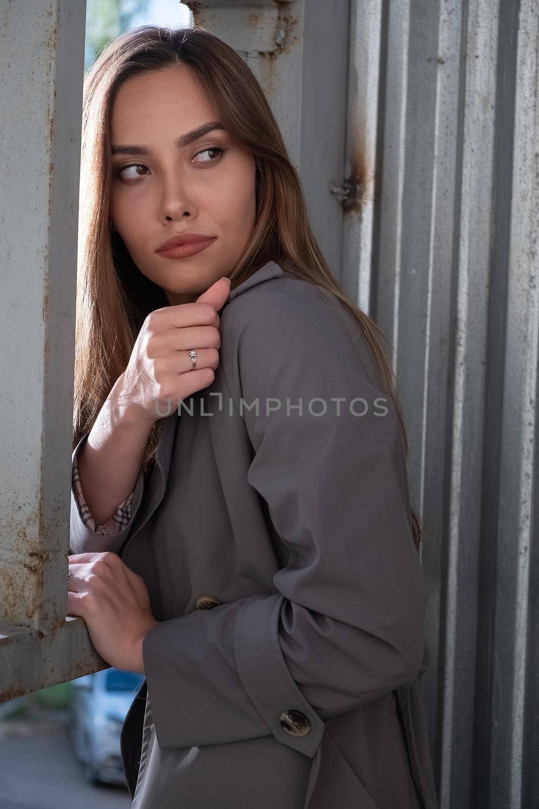 asian attractive model wearing gray trench coat standing in front of metal construction. outdoors portrait of young beautiful sensual stylish female