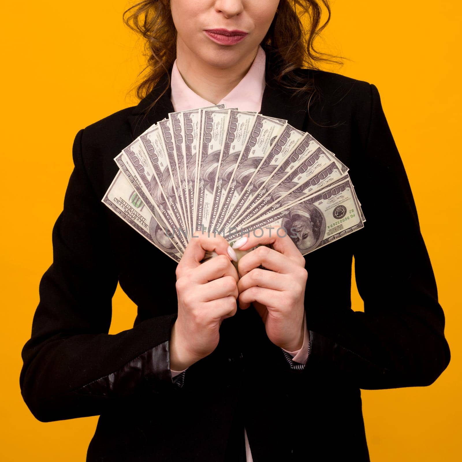 Woman showing a stack of money with her finger isolated on yellow background.