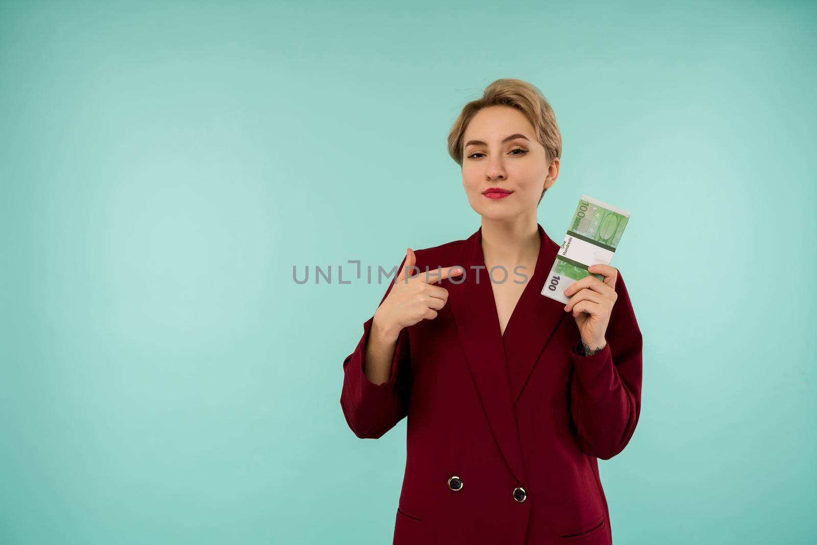 Portrait of beautiful young businesswoman pointing finger at money , on blue background - Image