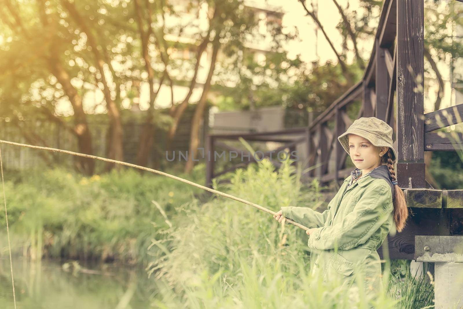 little fisher girl holdin a rod at a river near a bridge