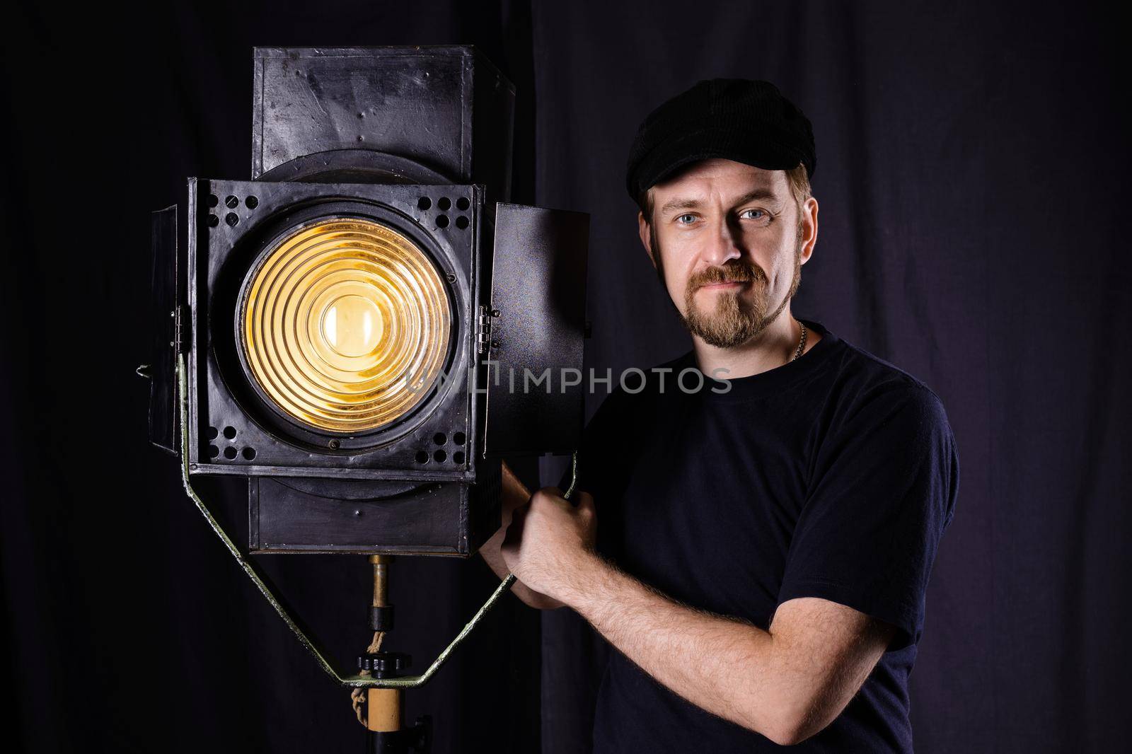 Man wearing a cap stands near a stage spotlight on black background
