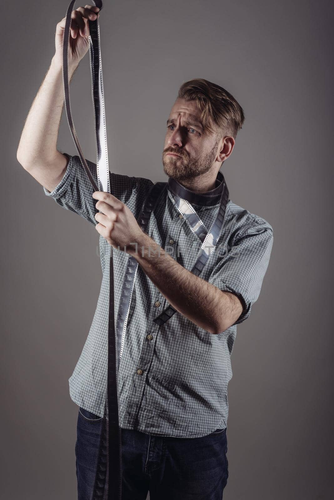 trendy man looks at the quality of the captured film on gray background.