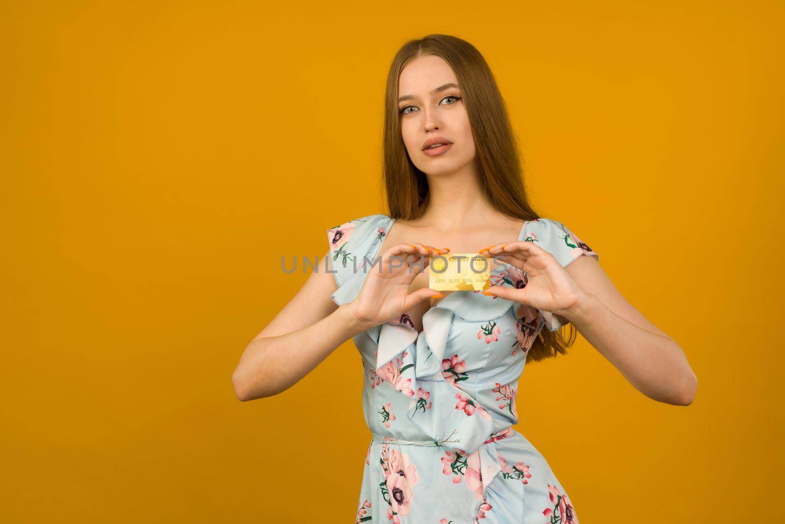 Photo of pleased young woman posing isolated over yellow wall background holding debit or credit card.