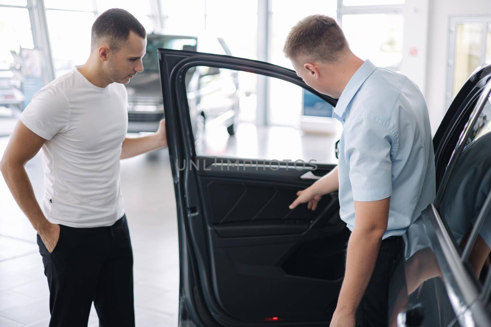 Salesperson selling cars at car dealership. Man choosing car in car showroom by Gritsiv