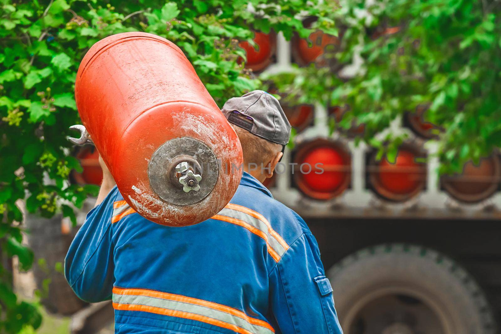 A male industrial worker walks with a gas cylinder to a gas car background.