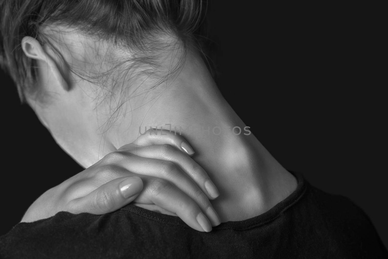 Unrecognizable woman touches her neck, pain in the neck, rear view