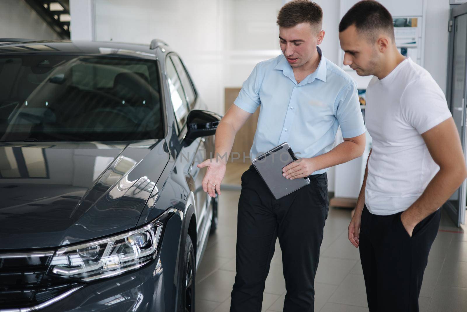 Salesperson selling cars at car dealership. Man choosing car in car showroom by Gritsiv