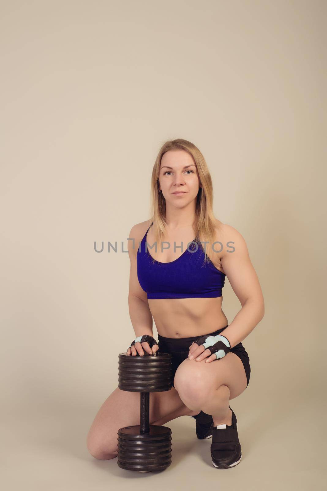 athletic woman bodybuilder sits with a heavy dumbbell by zartarn