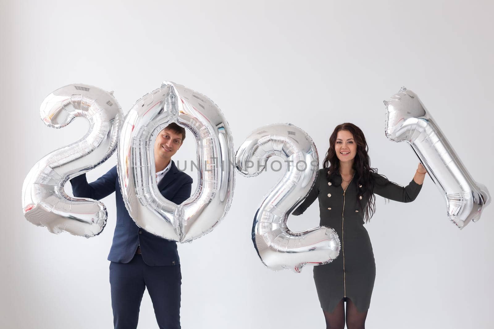 New year, celebration and holidays concept - love couple having fun with sign 2021 made of silver balloons for new year on white.
