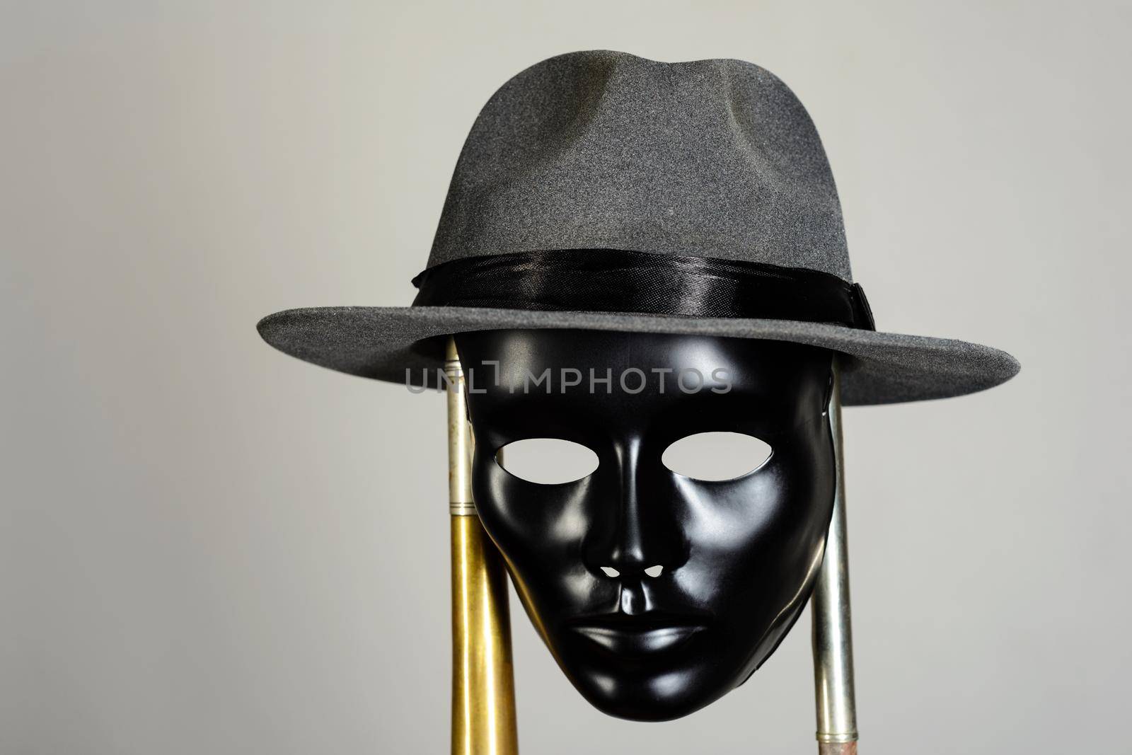 Black theater mask and hat hanging on a brass pipe on gray background with copy space. Social masking and mystery concept