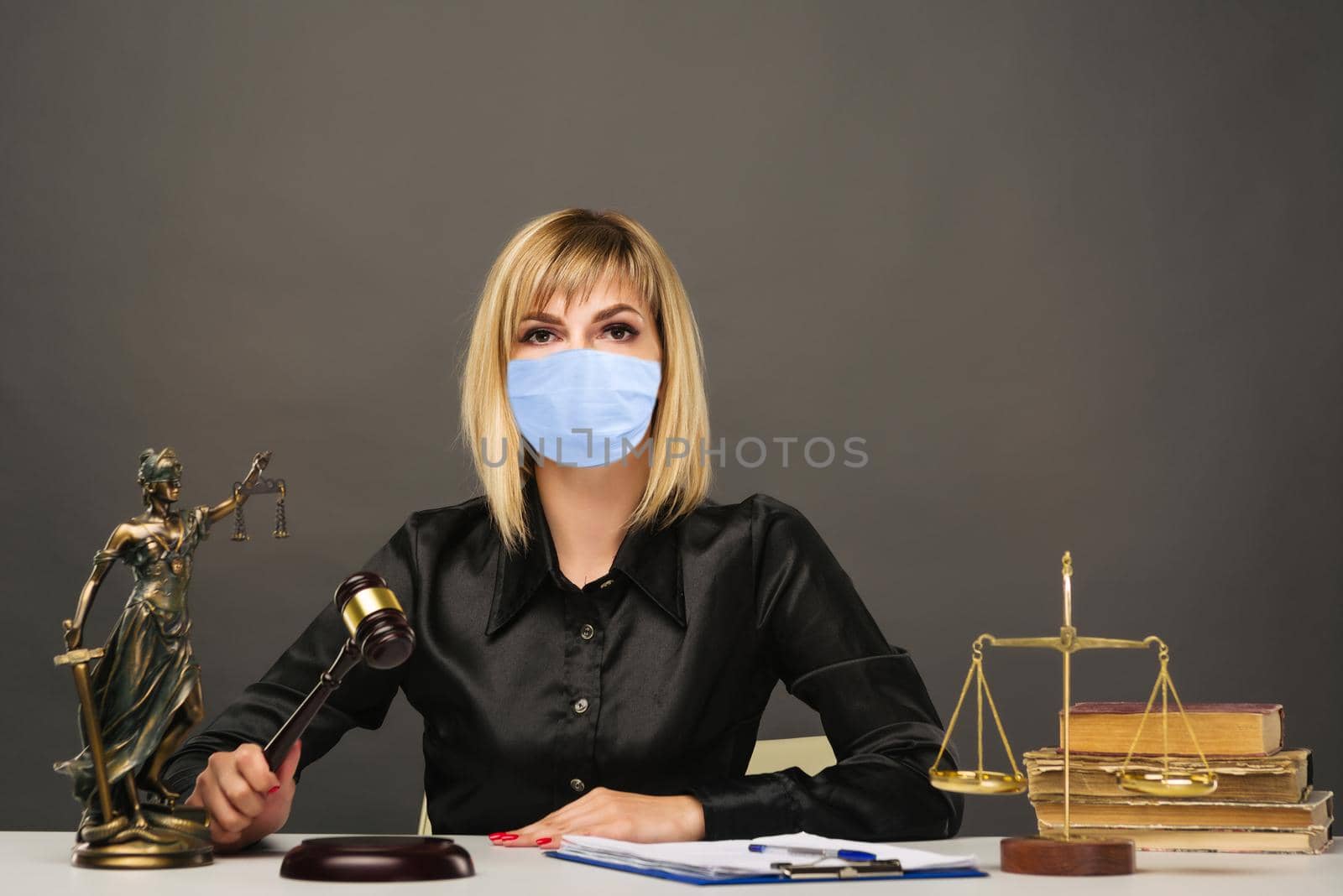 A young fair woman judge in protective mask works in her office. - image