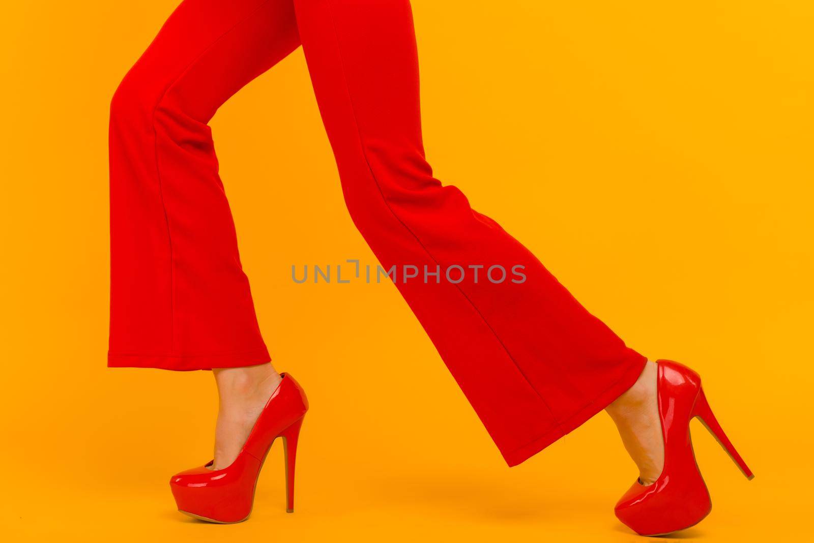 The business woman running somewhere hurrying up isolated on yelow background. Stylish red heels and pants on thin female legs