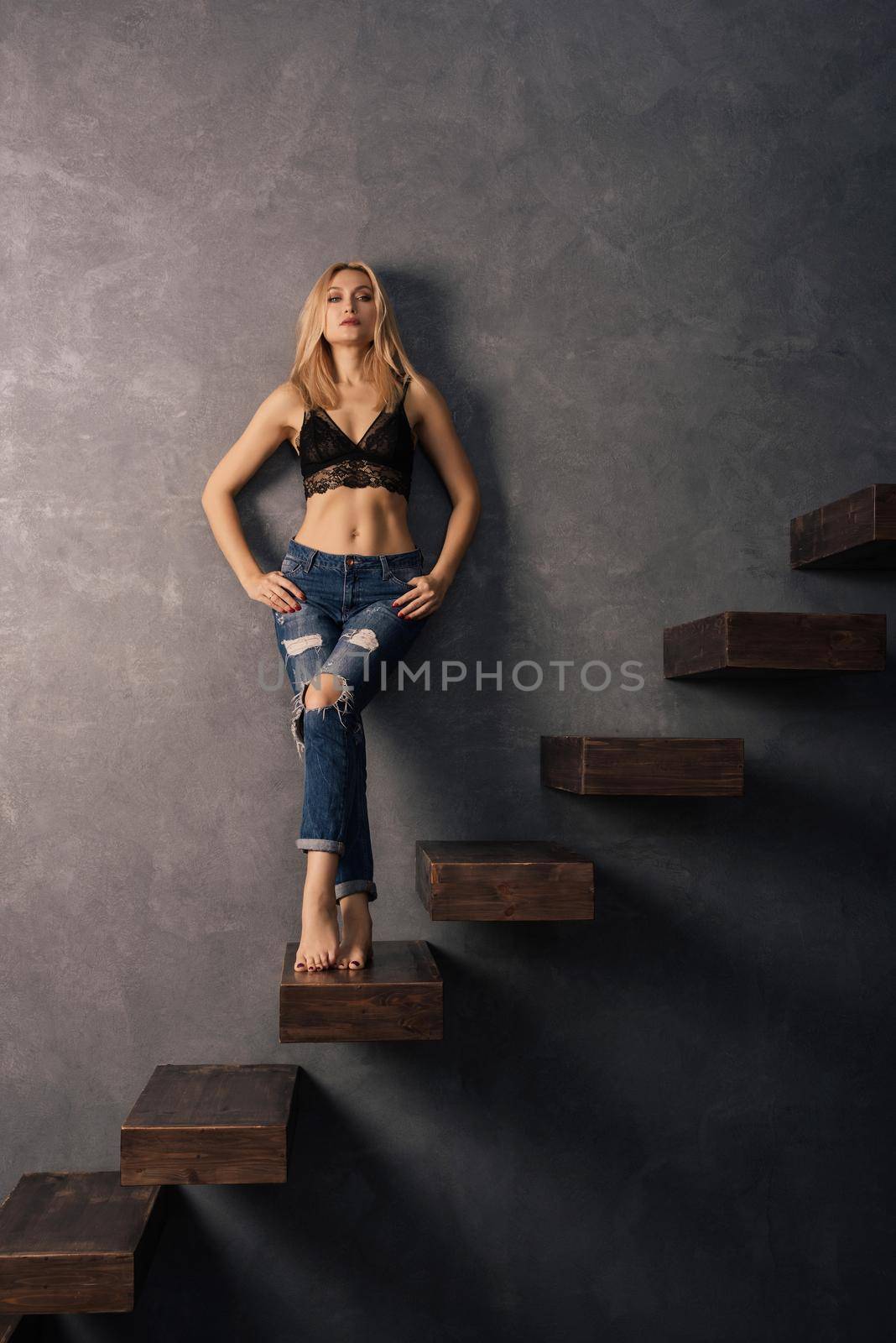 beautiful sensual woman in a bra and jeans standing on a wooden cantilever steps. Looking at camera