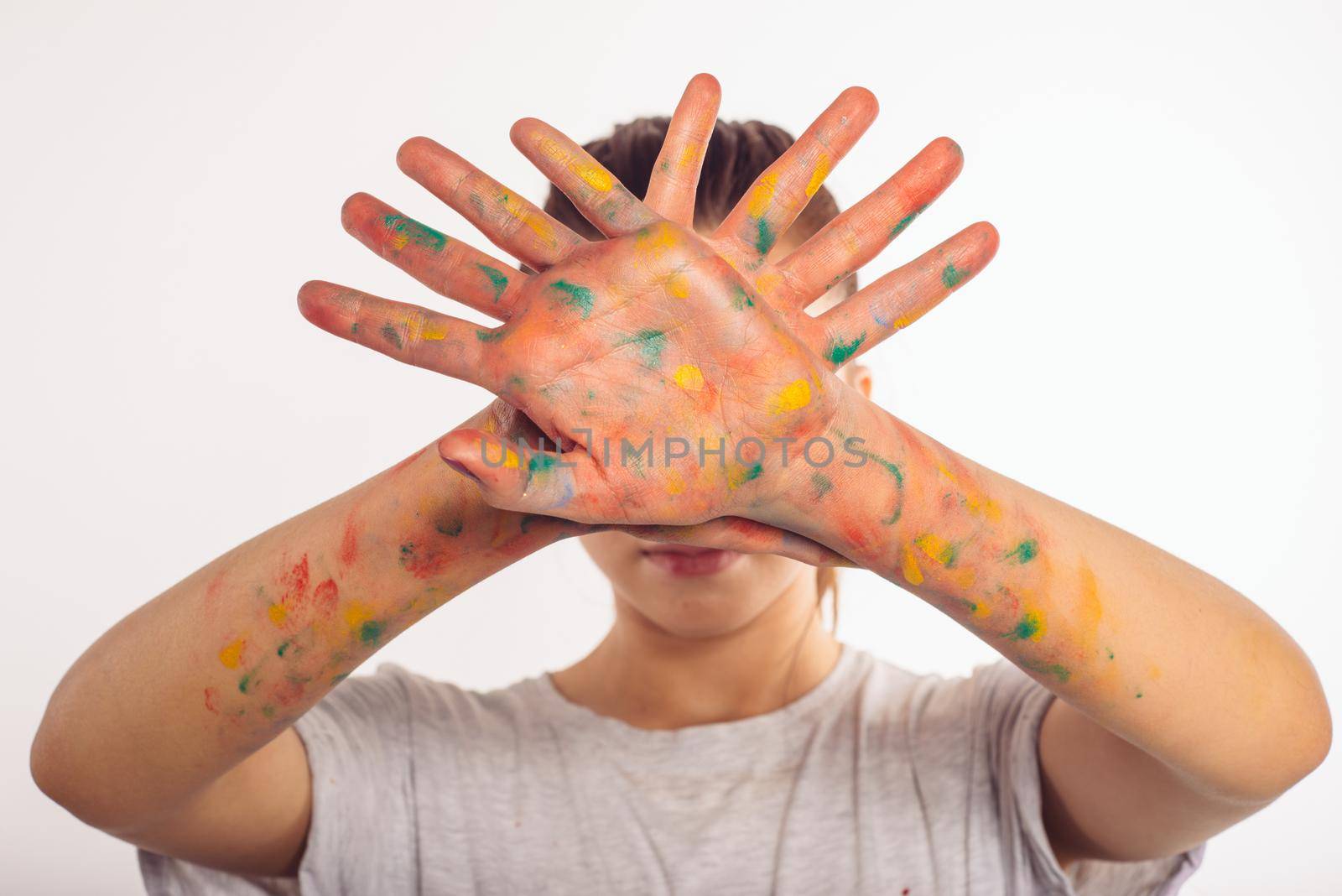 teenage girl covers her face with her palms in paint isolated on white