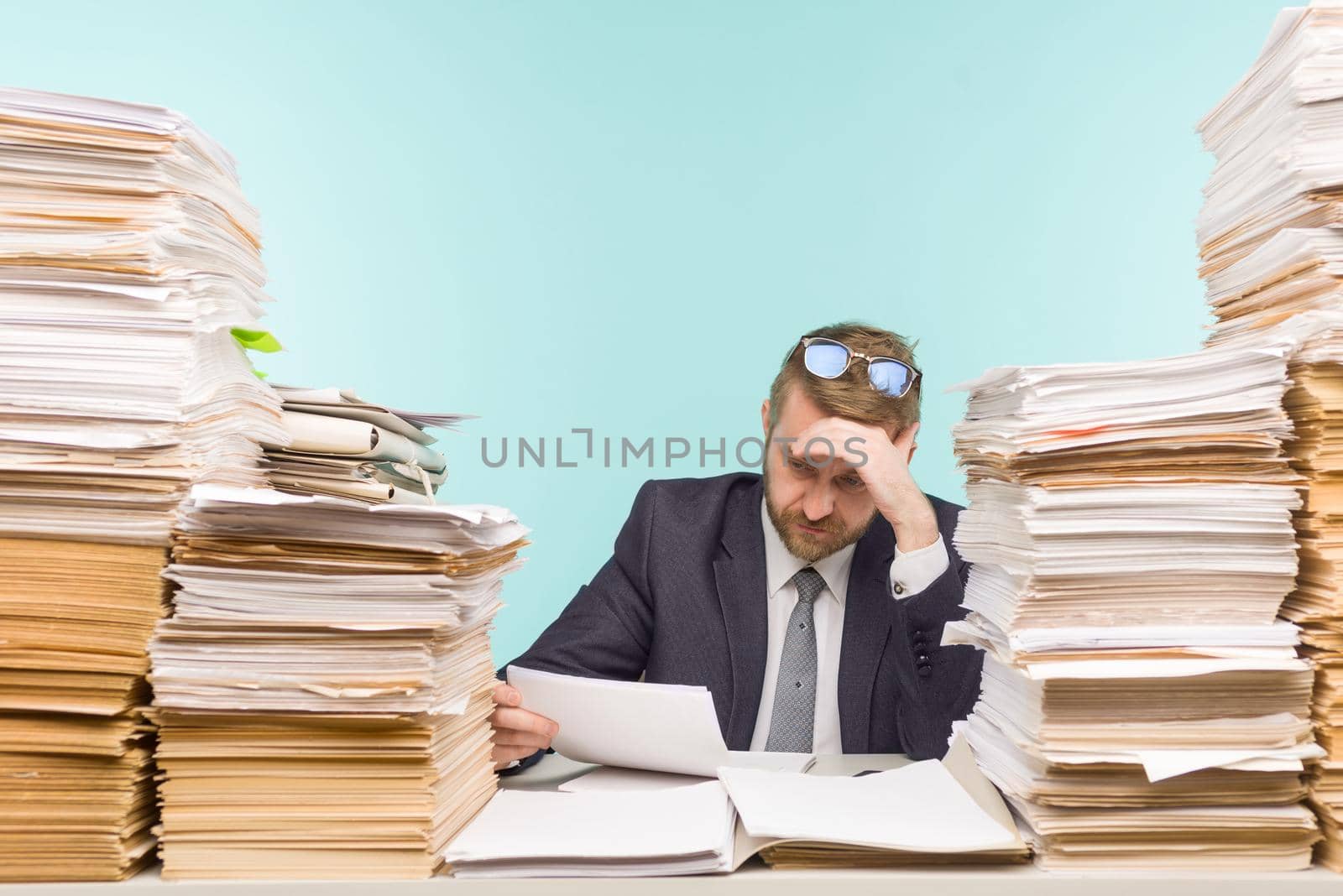 Business executive working in the office and piles of paperwork, he is overloaded with work - image