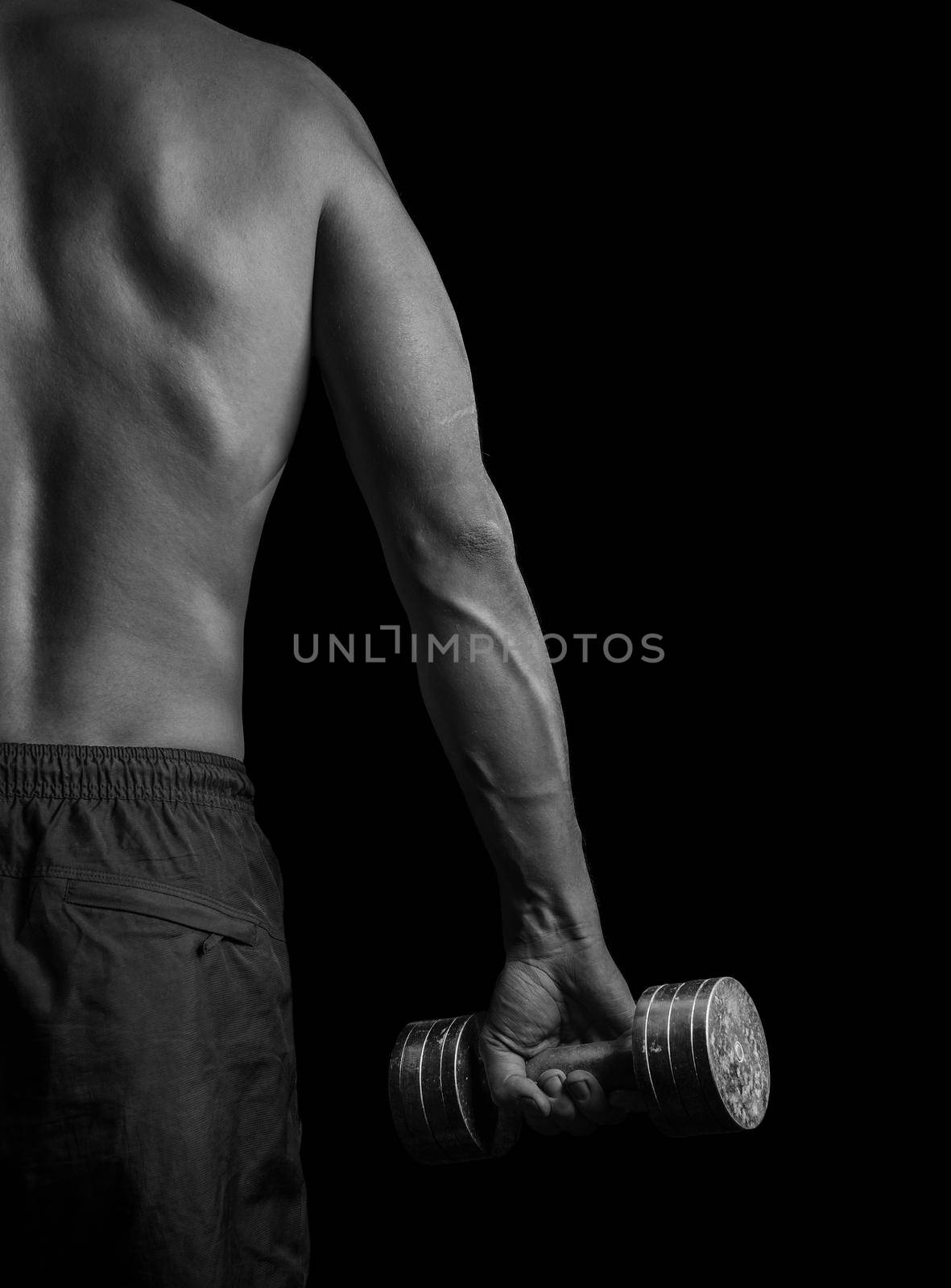 Unrecognizable muscular man exercises with dumbbell, rear view, monochrome image