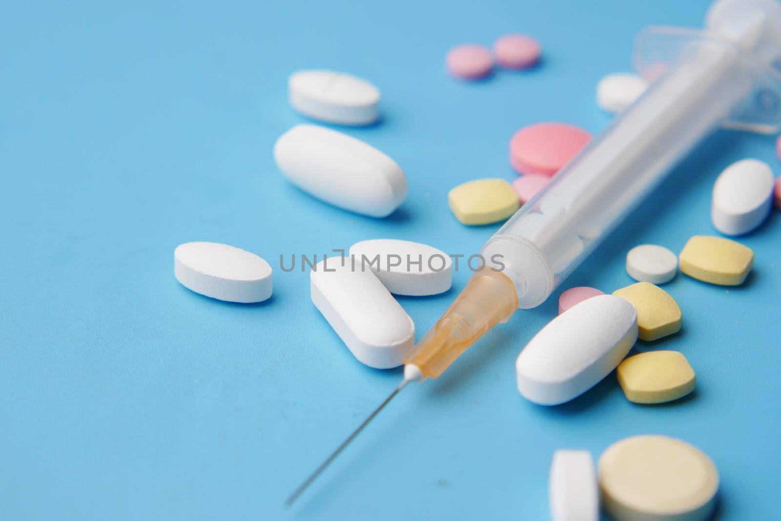 syringe and pills on blue background, close up .