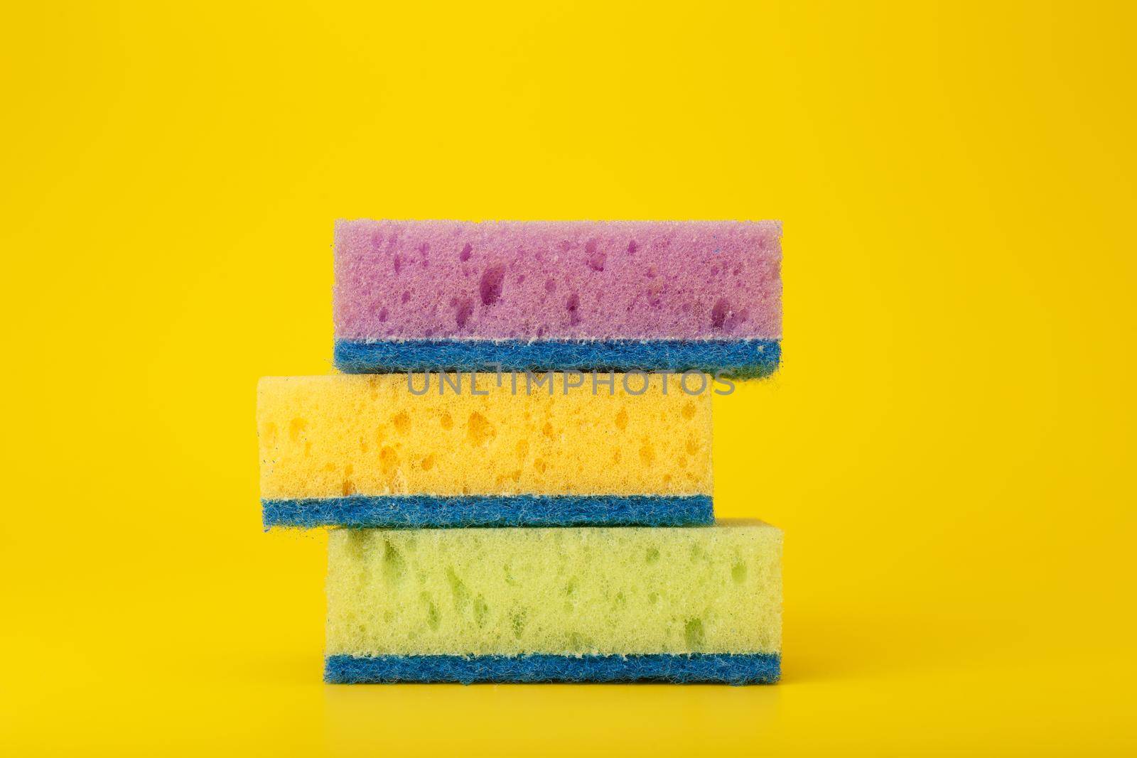 Close up of stack of three multicolored cleaning or kitchen sponges on bright yellow background by Senorina_Irina