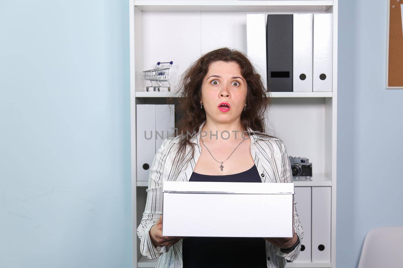 Concept of dismissal from work. Stunned woman with carton box with her stationery stuff, girl was fired from her job