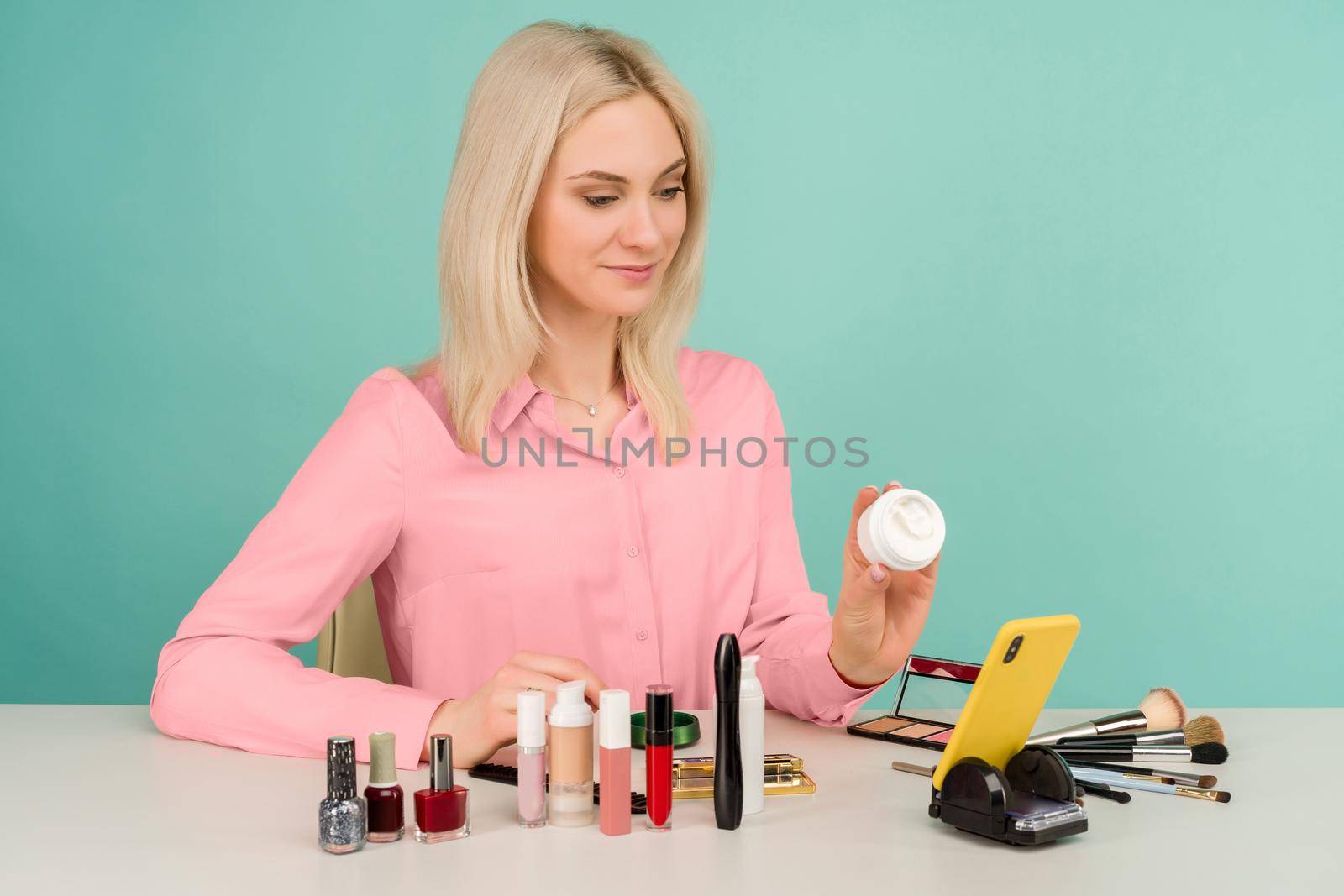Candid shot of cute young Caucasian woman blogger presenting beauty products and broadcasting live video to social network, showing anti-aging cream while recording everyday make up tutorial