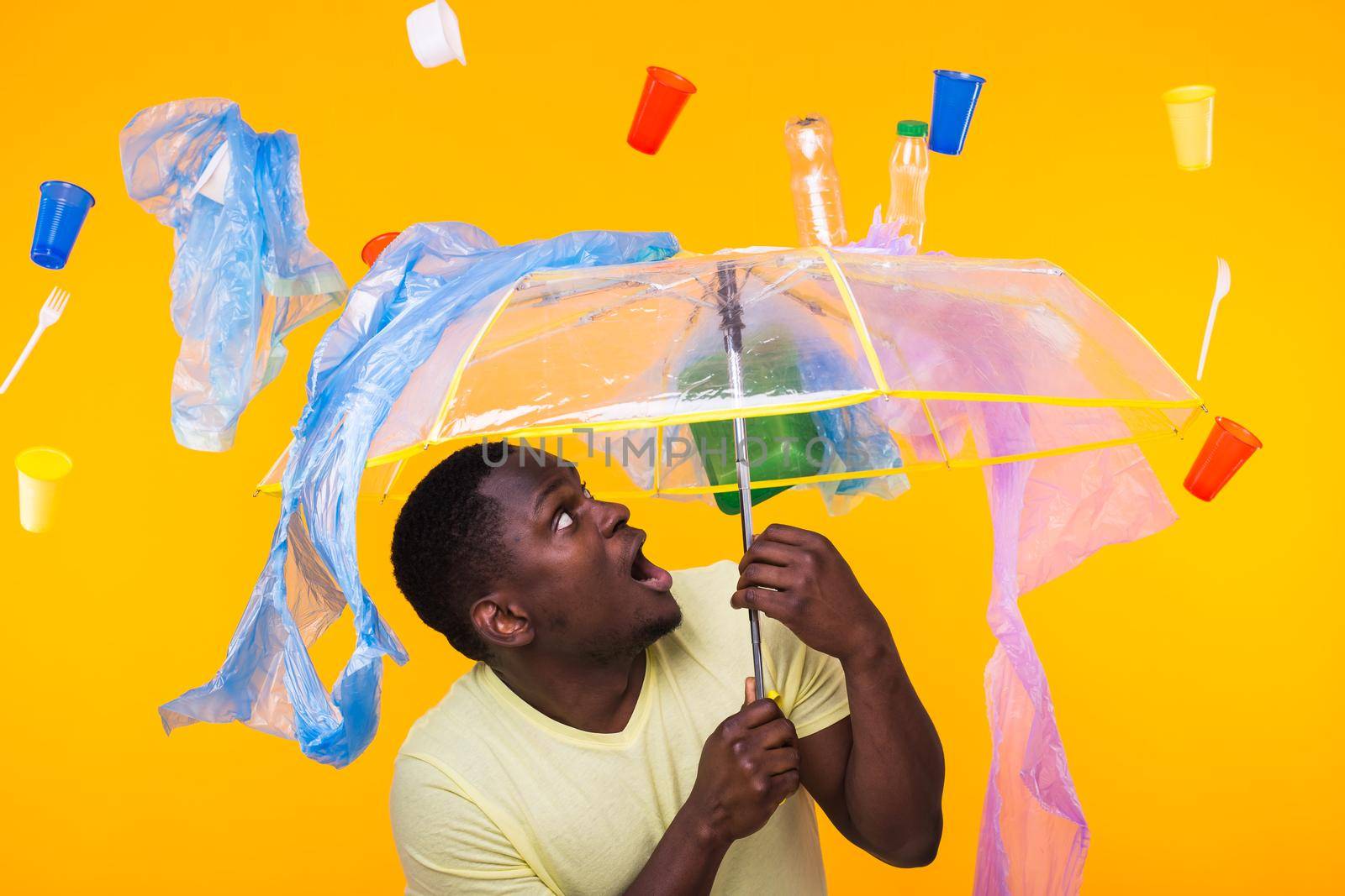 World Environment Day, plastic recycling problem and environmental disaster concept - Surprised african american man looking on trash on yellow.