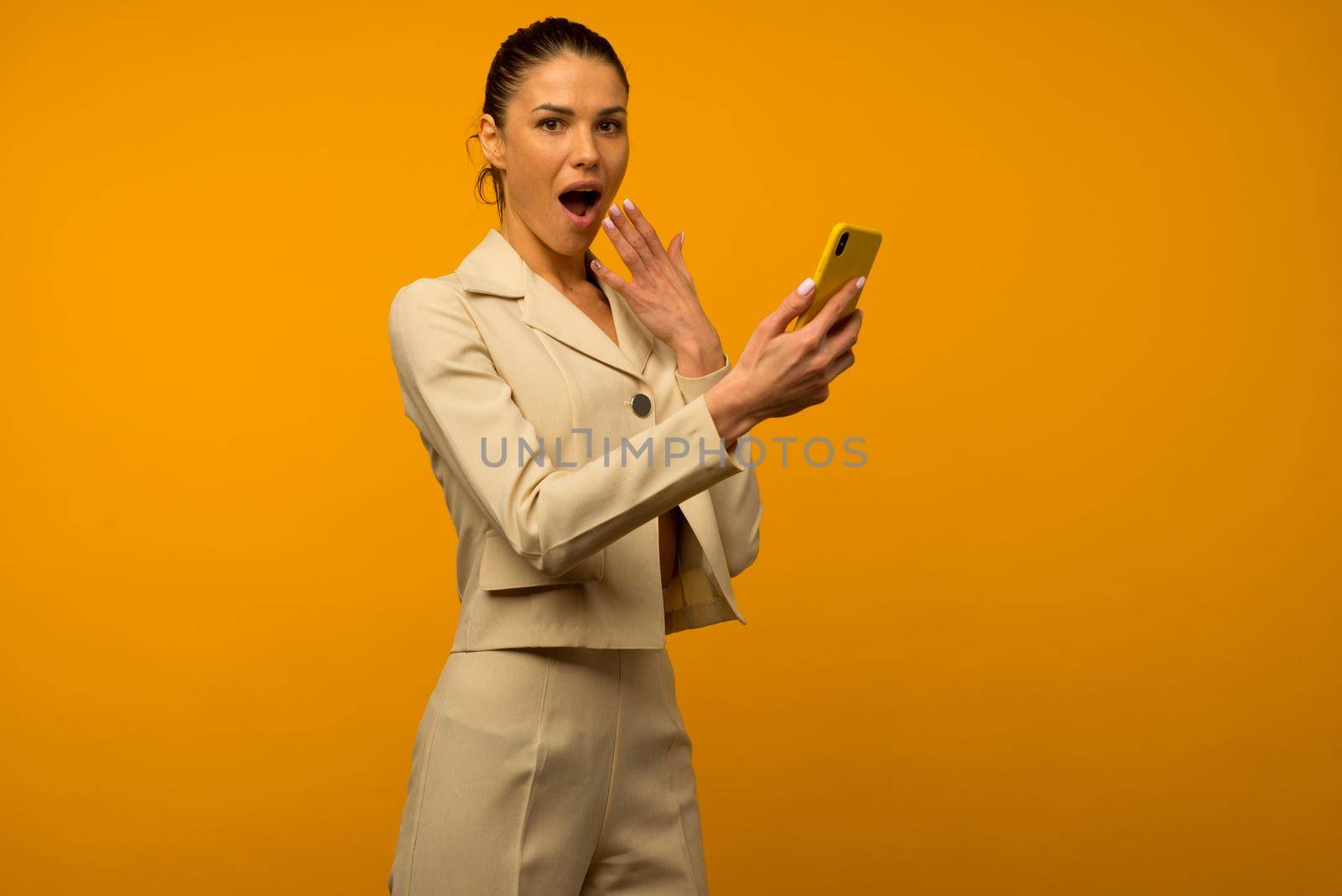 Young girl with facial skin problems posing with a smartphone on a yellow background.