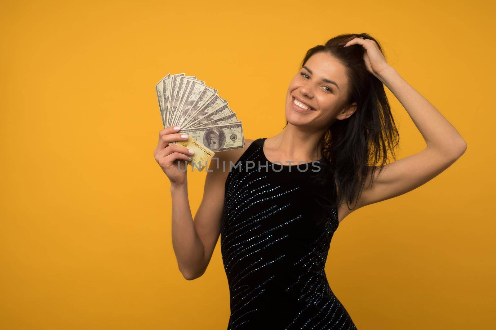 Photo of pleased happy young woman posing isolated over yellow wall background holding money and credit or debt card. by zartarn