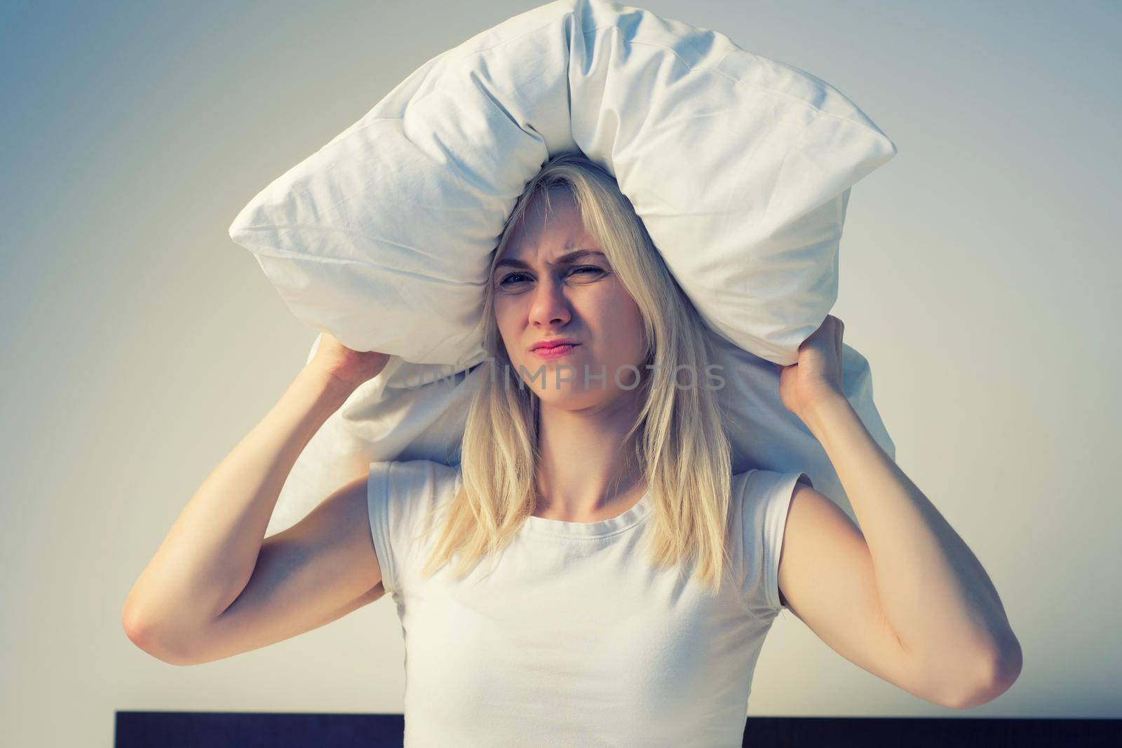 Young woman covering ears with pillow because of noise. - image toned