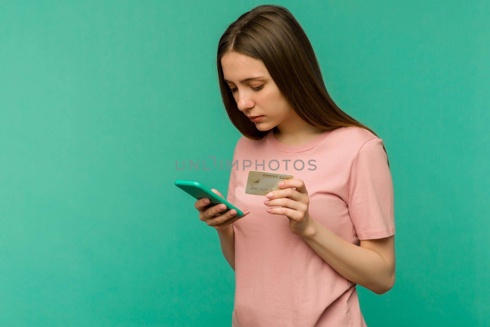 Photo of pleased happy screaming young woman posing isolated over blue wall background using mobile phone holding credit card. - image
