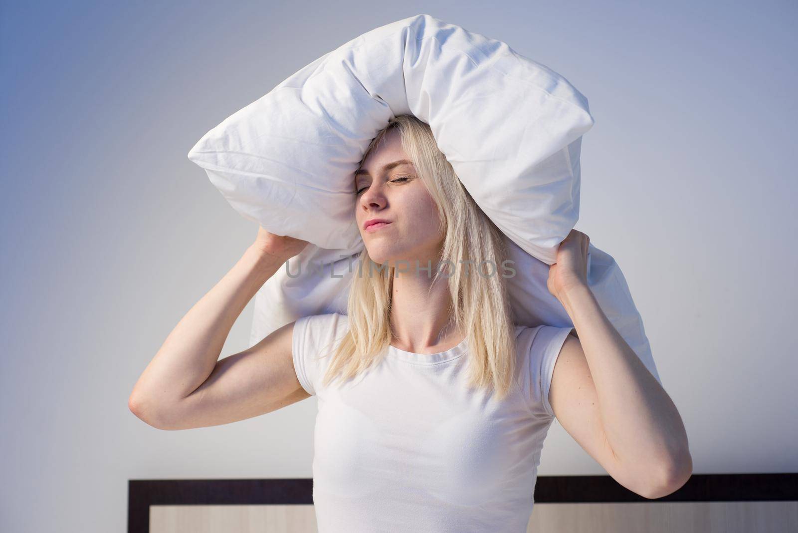Young woman covering ears with pillow because of noise. - image